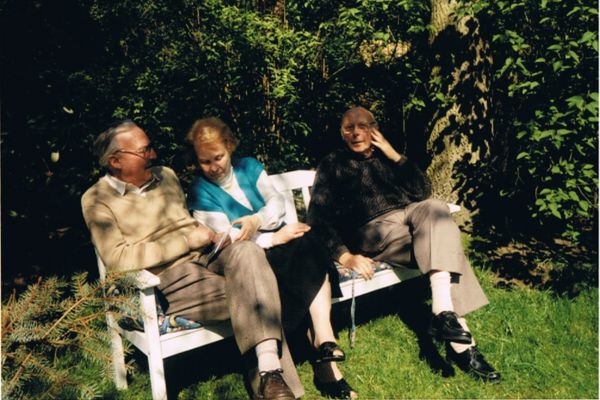 Auf einer weißen Bank im Garten haben sich die 3 Geschwister nach 50 Jahren viel zu erzählen.