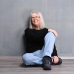 Sabine Wickel sitzt mit verschränkten Beinen auf dem Fußboden